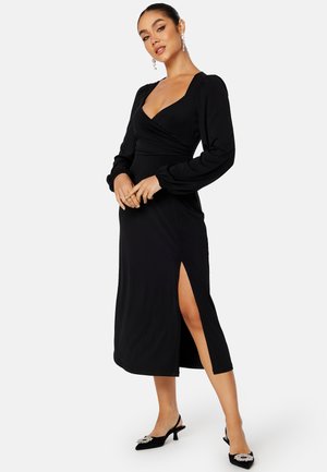 Zwart midi-jurk met een wikkelontwerp, lange pofmouwen en een zijhalve. Glad textuur met een elegante silhouet. Geaccentueerd met hakken.