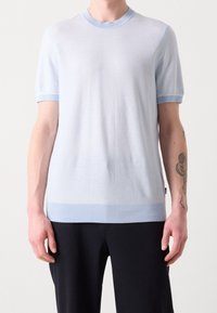 Jersey de punto de manga corta en azul claro con cuello y dobladillo acanalados. Textura suave, forma ajustada y sutiles acentos en contraste.
