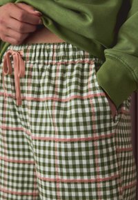 Green plaid pajama pants with white check pattern and pink accents. Elastic waistband with drawstring, side pockets, soft texture.