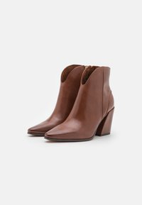 Bottines en cuir marron avec un bout pointu et un talon en bloc sculpté. Présente une ouverture courbée et des détails de coutures subtils.