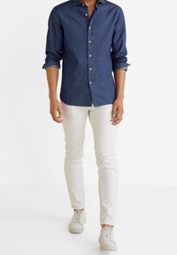 Ciemna koszula z denimu zapinana na guziki, białe wąskie spodnie i białe trampki. Koszula ma długie rękawy i klasyczny kołnierz.