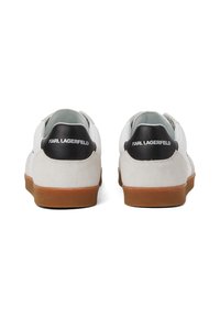 Valged nahktennisekingad halli seemisnaha kontsaga, must logo kontsas ja pruuni kummitald. Sile tekstuur koos minimalistlike disainielementidega.