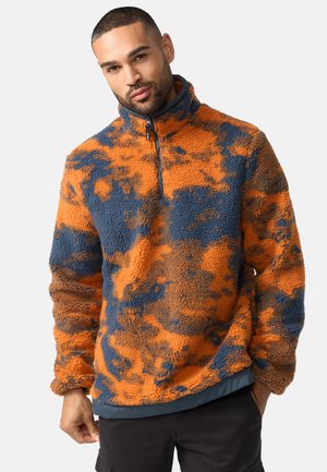 Fleece pullover in orange and blue camouflage pattern, featuring a high collar, half-zip front, and textured, plush fabric.
