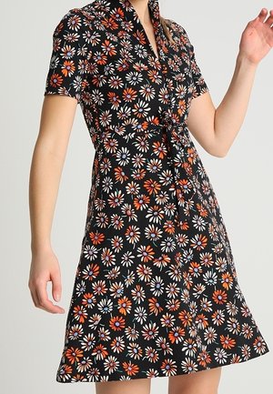 Lyhythihainen musta mekko, jossa on valkoisen, oranssin ja vihreän kukkakuosi. Mallissa on kaulus ja vyötäröä korostava leikkaus, joka luo istuvan siluetin.