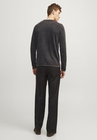 Mørkegrå langermet genser med rund hals, brukt sammen med svarte bukser. Stoffet virker mykt med en subtil tekstur.