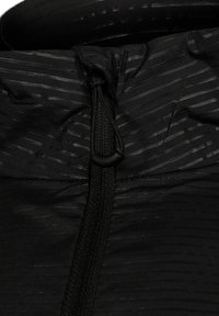 Svart jacka med en texturerad yta som har tunna, upphöjda ränder. Inkluderar en dragsnodd med en justerbar knapp vid kragen.