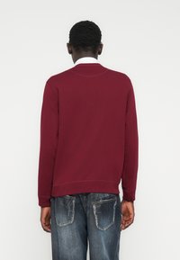 Bordo spalvos džemperis ilgomis rankovėmis ir ribotais rankogaliais, derinamas su mėlynais suplėšytais džinsais. Paprasta vienspalvė suknelė be raštų ar akcentų.