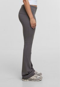 Leggings grises extensibles avec une taille haute, ajustés au niveau des hanches, s'évasant légèrement à l'ourlet, associés à des chaussures de sport grises claires.