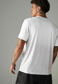 Hvid atletisk t-shirt med korte ærmer, med et tekstureret mesh-design. Inkluderer en rund halsudskæring og sideslids for forbedret bevægelighed.