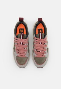 Sapatilhas com uma mistura de camurça cinza claro e oliva, com atacadores rosa e detalhes em riscas; forro laranja visível no interior.