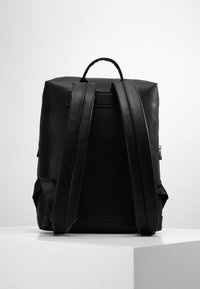 Svart läderryggsäck med breda justerbara remmar, ett handtag på toppen och en elegant, minimalistisk design. Slät yta med subtil sömnad.