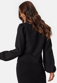 Zwarte, gestructureerde blouse met gepofte lange mouwen en een cropped design. Glad materiaal met een subtiele glans. Achteraanzicht toont naaddetails.