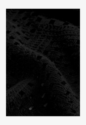 Svart texturerad tyg med en mjuk, plyschig yta som har ett mönster av geometriska former och små utskärningar, vilket skapar visuell intresse.