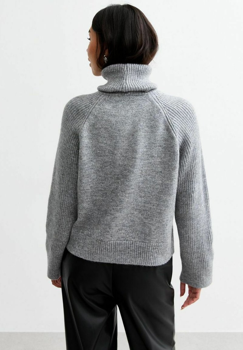 Szary sweter ze żebrowanym wzorem, z wysokim kołnierzem i rękawami raglanowymi. Posiada miękką teksturę i krótką formę, zestawiony z czarnymi spodniami.