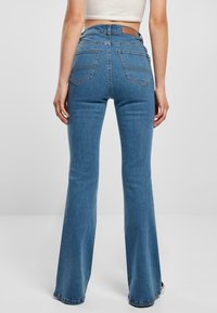 Jeans de mezclilla azules de campana con una cintura alta, costuras en contraste y dos bolsillos traseros, con una etiqueta de cuero marrón en la cintura.