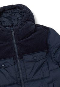 Giacca puffer blu navy con cappuccio in velluto a coste, chiusura con zip e tasche sul petto con bottone a pressione; presenta una texture trapuntata e un tessuto morbido.