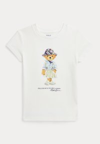 Camiseta de algodón blanca con un gráfico colorido de un oso con un sombrero de cuadros, camisa abotonada, falda y zapatillas, con el texto "Polo Bear by Ralph Lauren".