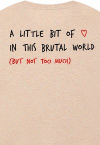 Lichtbeige katoenen T-shirt met korte mouwen en grote zwarte en rode tekst op de achterkant die een boodschap over liefde in een harde wereld uitdrukt.