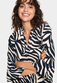 Mekko, jossa on laivastonsininen ja kerma-valkoinen zebra-kuvio, kauluksellinen neckline ja levenevät hihat, valmistettu kevyestä kankaasta.