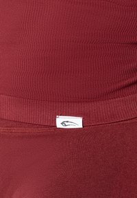 Bourgogne atletiske leggings med ribbet tekstur, der har en lille hvid etiket med en sort grafik på elastikken.