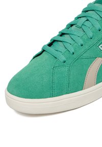 Zielony zamszowy sneaker z turkusowymi sznurowadłami, beżowym paskiem po boku oraz białą, fakturowaną gumową podeszwą, pokazany z bliska od strony palców.