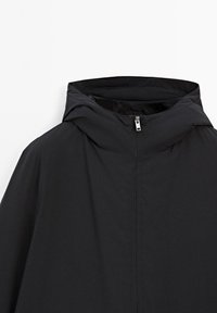 Schwarze Jacke mit hohem Kragen, Reißverschluss und glatter Textur. Das Design konzentriert sich auf Minimalismus ohne sichtbare Muster oder Akzente.