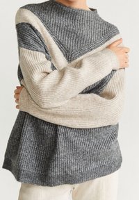 Pull en tricot avec un design en blocs de couleur gris et crème, texture côtelée et col montant. Coupe ample avec des manches longues.