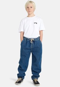 Losse spijkerbroeken van blauw denim met een elastische tailleband en trekkoord. Gecombineerd met een simpel wit T-shirt met een klein logo. Zwarte sneakers.