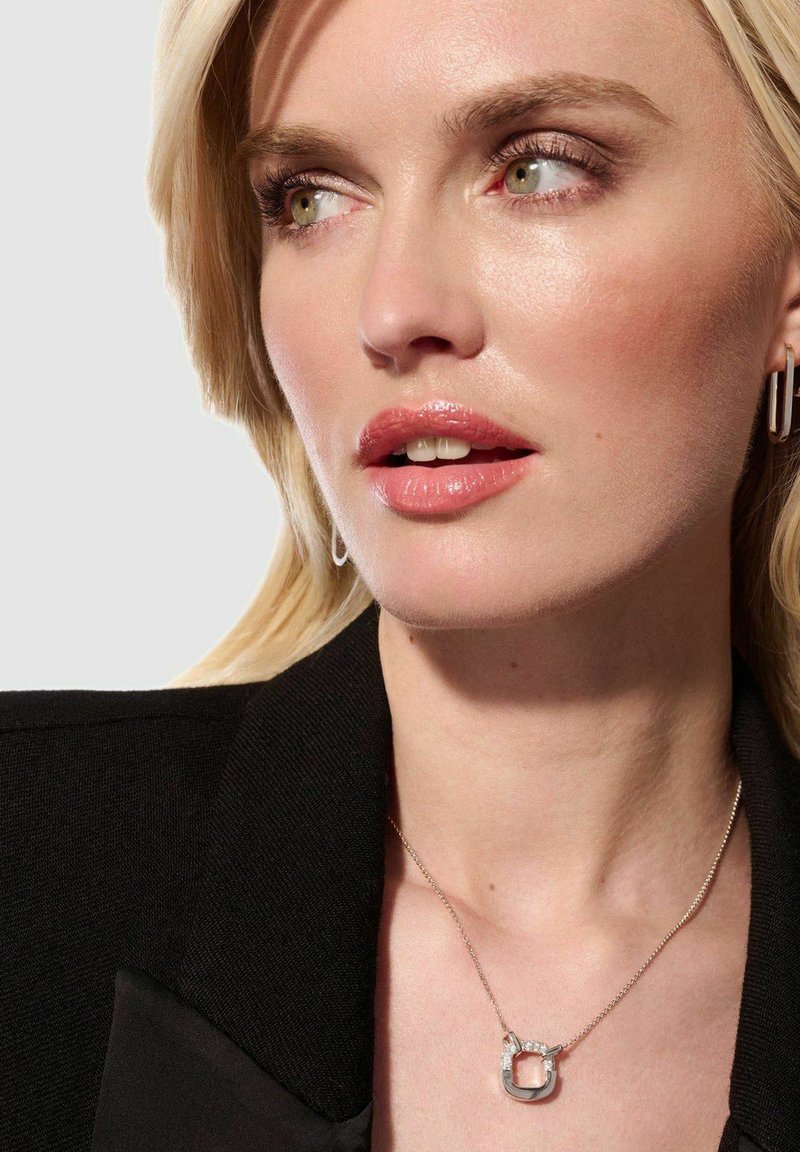 Silverhalsband med en fyrkantig berlock som har en klar stens accent, bärs med en svart blazer, framhävt mot en ljus bakgrund.