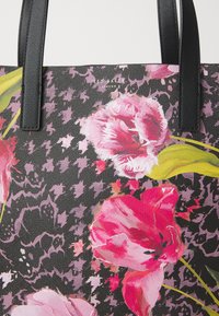 Bloemen-tas met roze en paarse tulpafdrukken op een zwart patroonachtergrond. Voorzien van zwart gestructureerde handvatten en logo-detail.