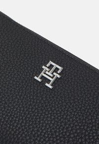 Schwarze Lederbörse mit strukturierter Oberfläche, mit einem silbernen Metallschriftzug in der Mitte.