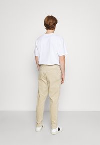 Pantalon en velours côtelé beige avec une coupe décontractée, poches arrière et un T-shirt blanc. Terminé avec des baskets blanches avec des accents noirs.