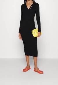 Černé pletené šaty s dlouhými rukávy, výstřihem do V a třemi knoflíky. V kombinaci se žlutou kabelkou a oranžovými sandály na pásky.