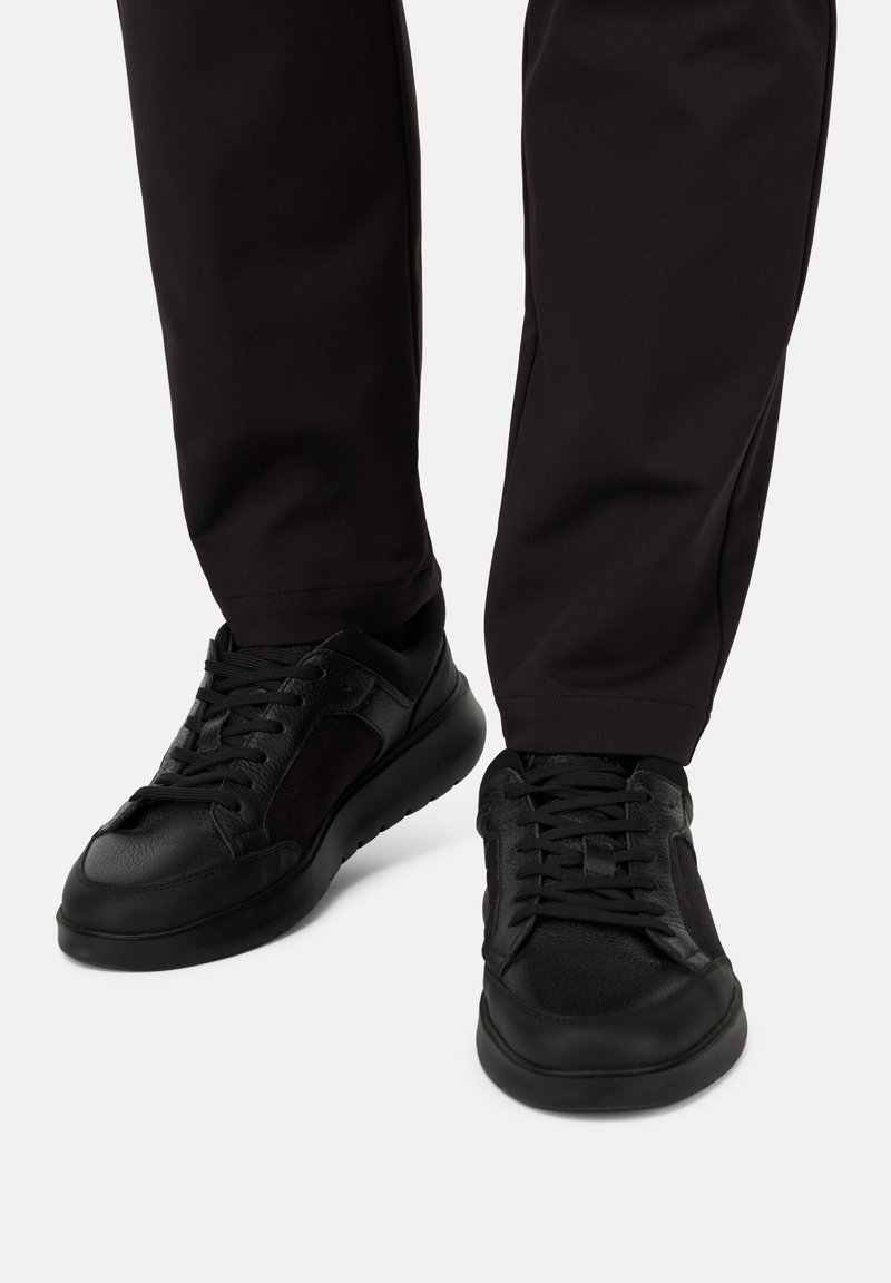 Črne superge z teksturirano usnje in mrežasto zasnovo, z okroglo konico, vezalkami na sprednji strani ter oblazinjeno, debelo podplatom.