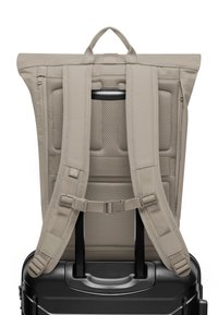 Beige reppu, jossa on pehmustetut olkahihnat kiinnitetty mustan matkalaukun kahvaan, esittäen hengittävää selkäpaneelia ja säädettävää rintakiinnikettä.