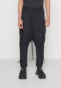 Schwarze Cargo-Hosen mit einem Kordelzugbund, mehreren Taschen und Knopfverschluss. Mit gerafften Knöchelbündchen und strukturiertem Stoff.