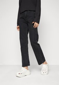 Jeans de mezclilla negra con pierna recta, combinados con zuecos blancos de plataforma que cuentan con agujeros de ventilación y una suela gruesa.