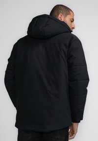 Schwarze Puffjacke mit Kapuze, versehen mit gesteppten Abschnitten und einer glatten Textur. Das Design umfasst einen hohen Kragen und elastische Bündchen.