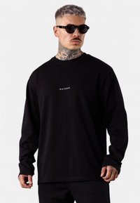 Schwarzes Langarm-T-Shirt aus weichem Stoff, mit einem kleinen weißen Textlogo "esteem." zentriert auf der Brust. Glatte Textur, lässige Passform.