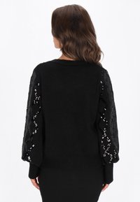 Czarny sweter z teksturowanej tkaniny i rękawami zdobionymi cekinami. Posiada okrągły dekolt oraz ściągacze przy mankietach. Elegancki, dopasowany krój.