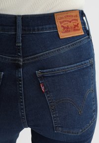 Dunkelblaue Jeans aus Denim mit hoher Taille, ausgestattet mit einem Leder-Logopatch und charakteristischem Stitching auf den hinteren Taschen.