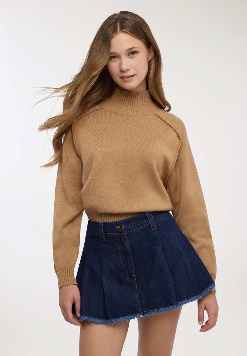 Maglione a coste marrone con collo a dolcevita abbinato a una gonna skater in denim scuro con orlo sfrangiato e tasche frontali.