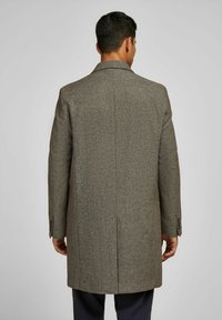 Bruine tweedjas met een gestructureerde afwerking, rechte snit, geknipte revers en twee rugventilaties. Beschikt over knoopsluitingen aan de mouwen en een getailleerd ontwerp.