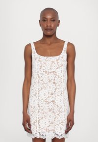Vit spetsklänning med fyrkantig halsringning, blommönster, ärmlös design och scalloped nederdel. Lätt material och figurnära passform.