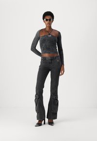 Haut noir à manches longues avec un col arrondi et un design de bretelles croisées, associé à un jean noir évasé avec des poches zippées et des accents froncés.