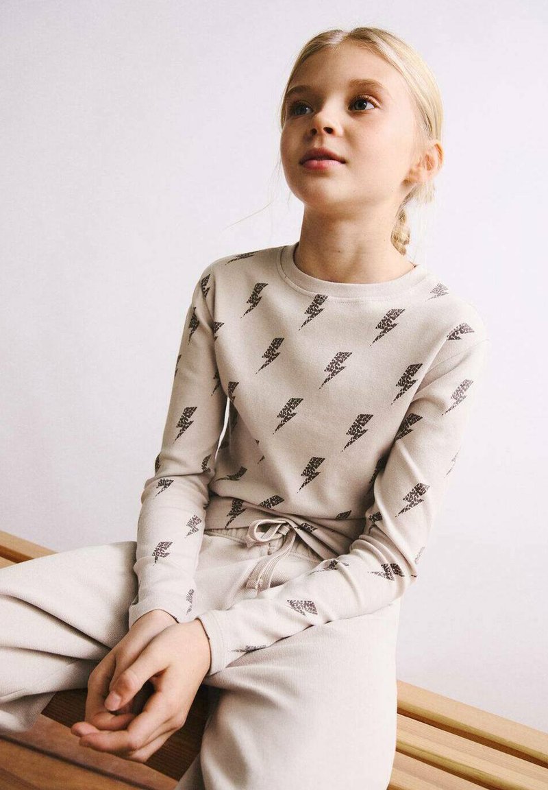 Haut à manches longues beige clair avec un motif d'éclair foncé, associé à un pantalon beige assorti avec une ceinture à cordon.