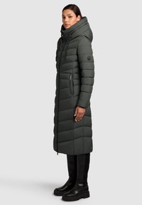 Langer Steppmantel in Dunkelgrün mit Kapuze, Reißverschlusstaschen, horizontalen Steppnähten und einem schlanken, isolierten Design.