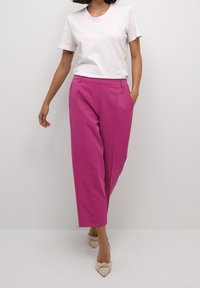 Fuchsia byxor med skräddarsydd passform, med sidofickor och en slät textur. Sammanfogat med en enkel vit t-shirt och beigefärgade spetsiga skor.