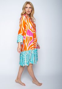 Kleurrijke jurk met gedurfde oranje, roze en turquoise patronen. Vloeiende stijl, kniehoogte met lange mouwen en een gerimpelde onderkant.