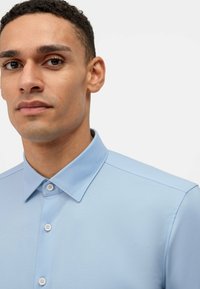 Camicia azzurra a maniche corte con colletto strutturato. Presenta una chiusura con bottoni e una texture liscia. Design semplice con dettagli di cucitura sottili.